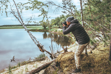A man with a pick-up in a gray jacket, photographs nature on the banks of the river, in the forest