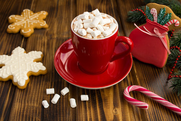 Hot chocolate with marshmallows in the red cup and Christmas gingerbreads  on the brown wooden background