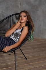 Fototapeta premium Closeup woman portrait. Young contented fashionable girl posing in sitting in a chair. Fashion.