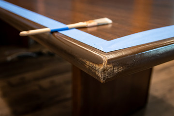 Paintbrush on edge of conference table; prepped with painter's tape for fresh coat of enamel paint