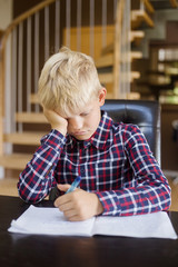 Sad schoolboy writing to notebook at home. Homework. Education, childhood and people concept