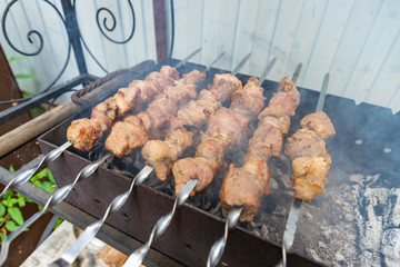 Shashlik or shashlyk preparing on a barbecue grill over charcoal. Grilled cubes of pork meat on metal skewer. Meat on skewers is roasted on fire