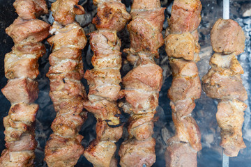 Shashlik or shashlyk preparing on a barbecue grill over charcoal. Grilled cubes of pork meat on metal skewer. Meat on skewers is roasted on fire