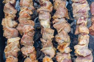 Shashlik or shashlyk preparing on a barbecue grill over charcoal. Grilled cubes of pork meat on metal skewer. Meat on skewers is roasted on fire