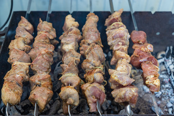 Shashlik or shashlyk preparing on a barbecue grill over charcoal. Grilled cubes of pork meat on metal skewer. Meat on skewers is roasted on fire