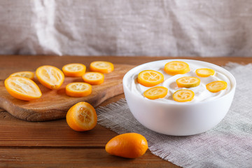 greek yogurt with kumquat pieces in a white plate on a brown wooden background