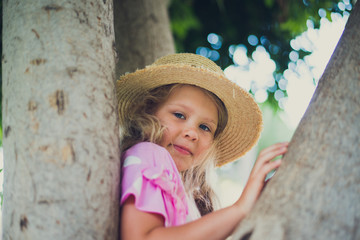 candid portrait of 7 y.o. girl in straw hat posing at the tree