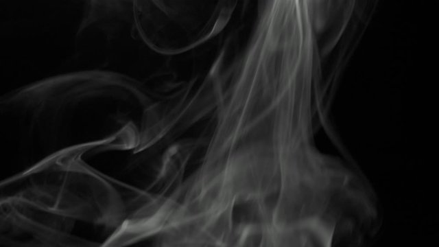 Clouds of gray smoke slowly rising graceful twists upward. Black and white cigar smoke blowing from bottom to top. Close-up, isolated on black background