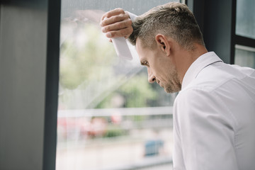 upset man standing near window and holding smartphone