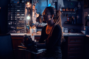 Portrait of young woman with dreadloks and glasses which is sitting at her tattoo studio.