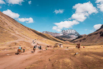 Tourists walking to Vinicunca Rainbow Mountain through stunning barren mountain landscape, Peru