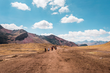 Tourists walking to Vinicunca Rainbow Mountain through stunning barren mountain landscape, Peru