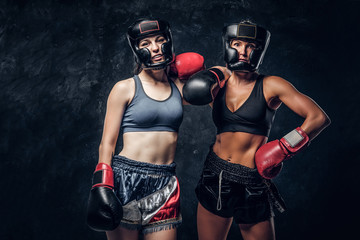 Experienced boxing trainer and her young student are posing for photographer at dark photo studio.