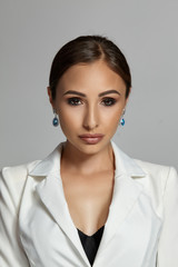 Close up portrait of a brunette model girl with professional evening make-up, wearing a white jacket with black bra, posing on gray background.