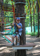 Fototapeta na wymiar Young boy passing the cable route high among trees, extreme sport in adventure park.