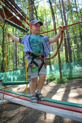 Young boy passing the cable route high among trees, extreme sport in adventure park.