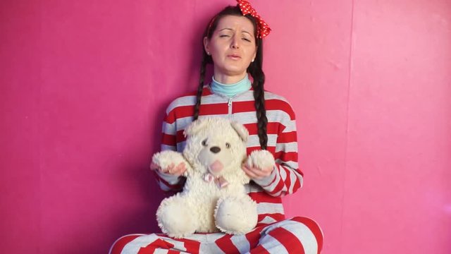 A woman in striped pyjamas. A grown girl with two pigtails. A grown woman behaves like a child. Girl with a bow on her head. Girl holding a Teddy bear.