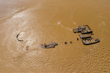 Aerial drone view of rusting hulls of abandoned ships in a brown, muddy river (River Severn)