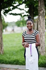 Young african american female doctor hold white coat on hand with a stethoscope posed outdoor.