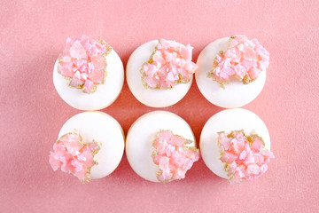 Minimalistic composition with bunch of white french macaron sweets with pink crystal shaped marmalade decoration over grunged concrete texture background. Top view, close up, flat lay, copy space.