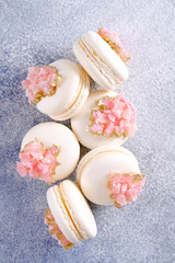 Minimalistic composition with bunch of white french macaron sweets with pink crystal shaped marmalade decoration over grunged concrete texture background. Top view, close up, flat lay, copy space.