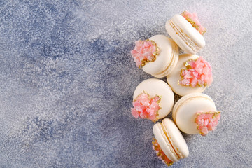 Minimalistic composition with bunch of white french macaron sweets with pink crystal shaped marmalade decoration over grunged concrete texture background. Top view, close up, flat lay, copy space.