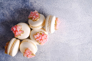 Minimalistic composition with bunch of white french macaron sweets with pink crystal shaped marmalade decoration over grunged concrete texture background. Top view, close up, flat lay, copy space.
