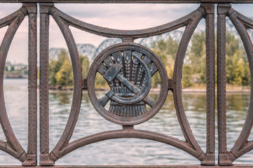 old iron fence on the waterfront with a medallion in the form of a hammer and sickle against wheat ears