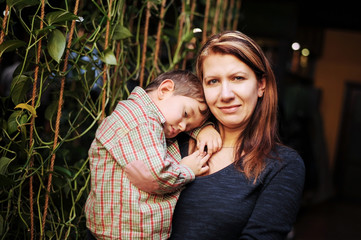 A woman holds in her hands a little boy who falls asleep in her arms. The boy rested with his mother in a cafe, had a good lunch and wanted to sleep