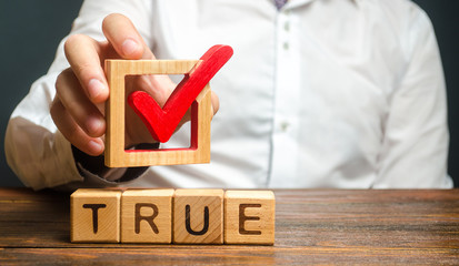 A man holds a red check mark over word True. Confirm the veracity and truth. Fight against fake...