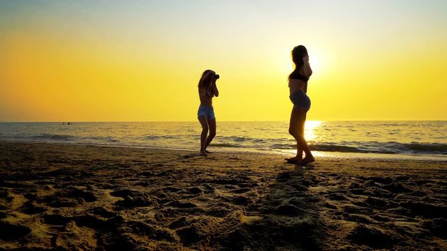 Photographer teen taking photos of female model on beach at sunset. Romantic photo session