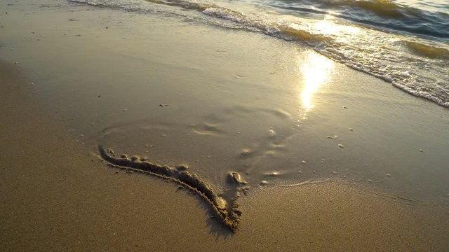 Summer romantic vacation concept of hearth on sand being washed by sea waves at sunset