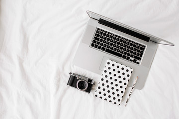 Laptop, notes writing and camera on white bed work at home concept. Top view of a desk working.
