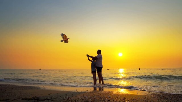 Father And Son Flying Kite on Sea Coast with nice Orange Sky Sunset. Steadicam Shot