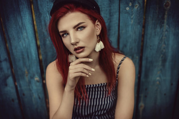 Fototapeta premium Young fashionable woman in clothes in a strip and red hair, posing on a blue background on the street.