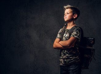 Pensive little kid is standing at dark photo studio while posing for photographer.