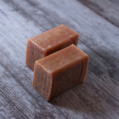 two pieces of brown natural soap on a wooden surface.
