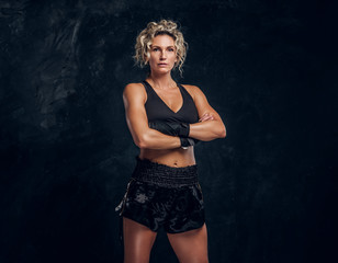 Fototapeta na wymiar Experienced female boxer is posing for photographer at dark photo studio with crossed hands.