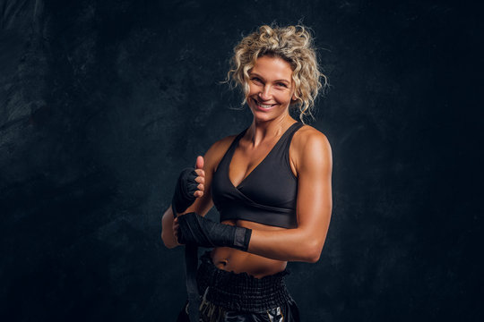 Happy smiling female boxer is posing for photographer at dark photo studio.