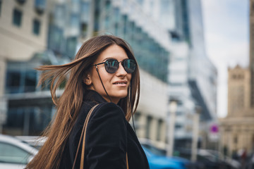 Young beautiful stylish girl in Sunglasses walking on street. Close up portrait of woman is turn around at camera and smiles. Female playfully looks at the camera.