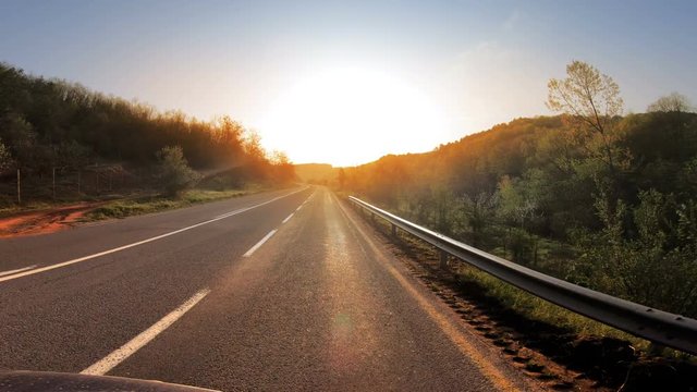 POV Driving on highway toward shining sun at spring sunrise