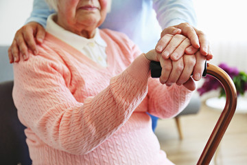 Mature female in elderly care facility gets help from hospital personnel nurse. Senior woman w/ aged wrinkled skin & care giver, hands close up. Grand mother everyday life. Background, copy space.