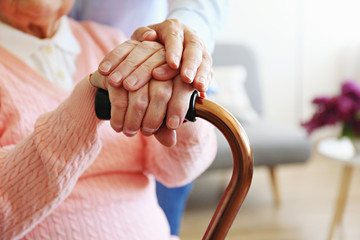Mature female in elderly care facility gets help from hospital personnel nurse. Senior woman w/ aged wrinkled skin & care giver, hands close up. Grand mother everyday life. Background, copy space.