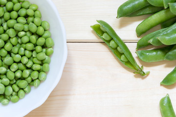 Peeled grean peas in white bowl on wooden table. Background with copy space.
