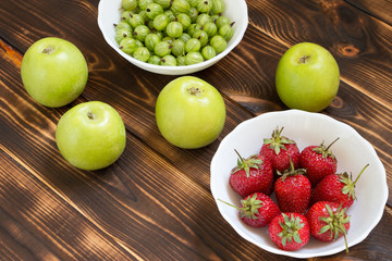 Natural organic healthy food. Green whole juicy apples, gooseberries and strawberries in white bowls on rustic wooden table.