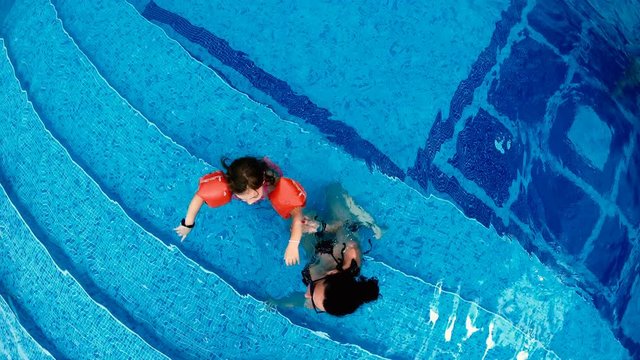 Aerial view of mother and little girl with arm bands relaxing in luxury pool, slow motion
