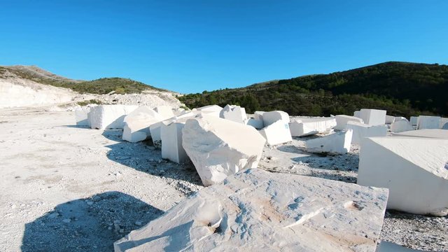 Walk POV at industrial marble quarry site with huge marble blocks