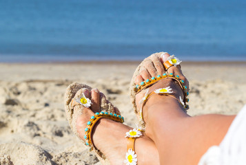 Fototapeta na wymiar Holidays at sea background with copy space. Female feet shod in sandals lay on golden sand near seashore.