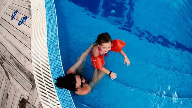Top view of happy family, mother and daughter with arm bands smiling and splashing water to camera, slow motion