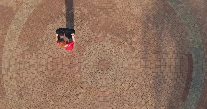 Elegant man in a black suit and a woman in red dance on the square in summer, tango, latina. Synchronous steps, movements. Circular motion of the camera. View from copter. Top view.